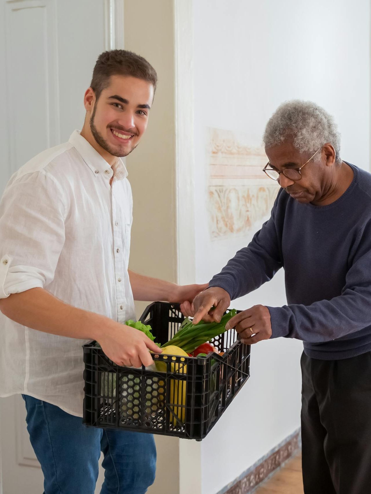 A Man Holding a Plastic Crater while Assisting an Elderly Man