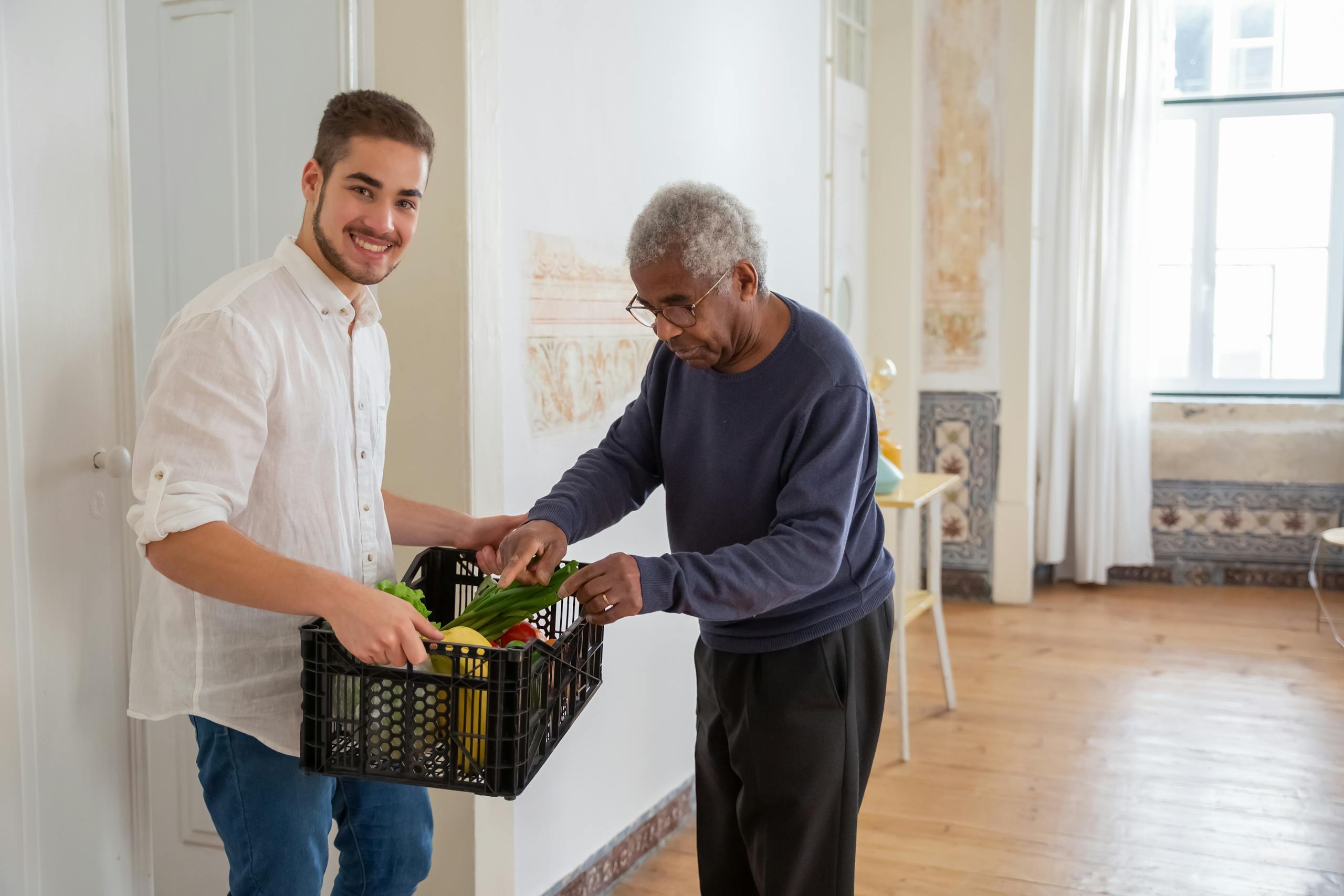 A Man Holding a Plastic Crater while Assisting an Elderly Man