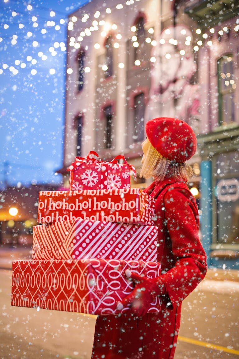 Woman carrying red holiday gifts in snowy city street, embracing winter festivities.