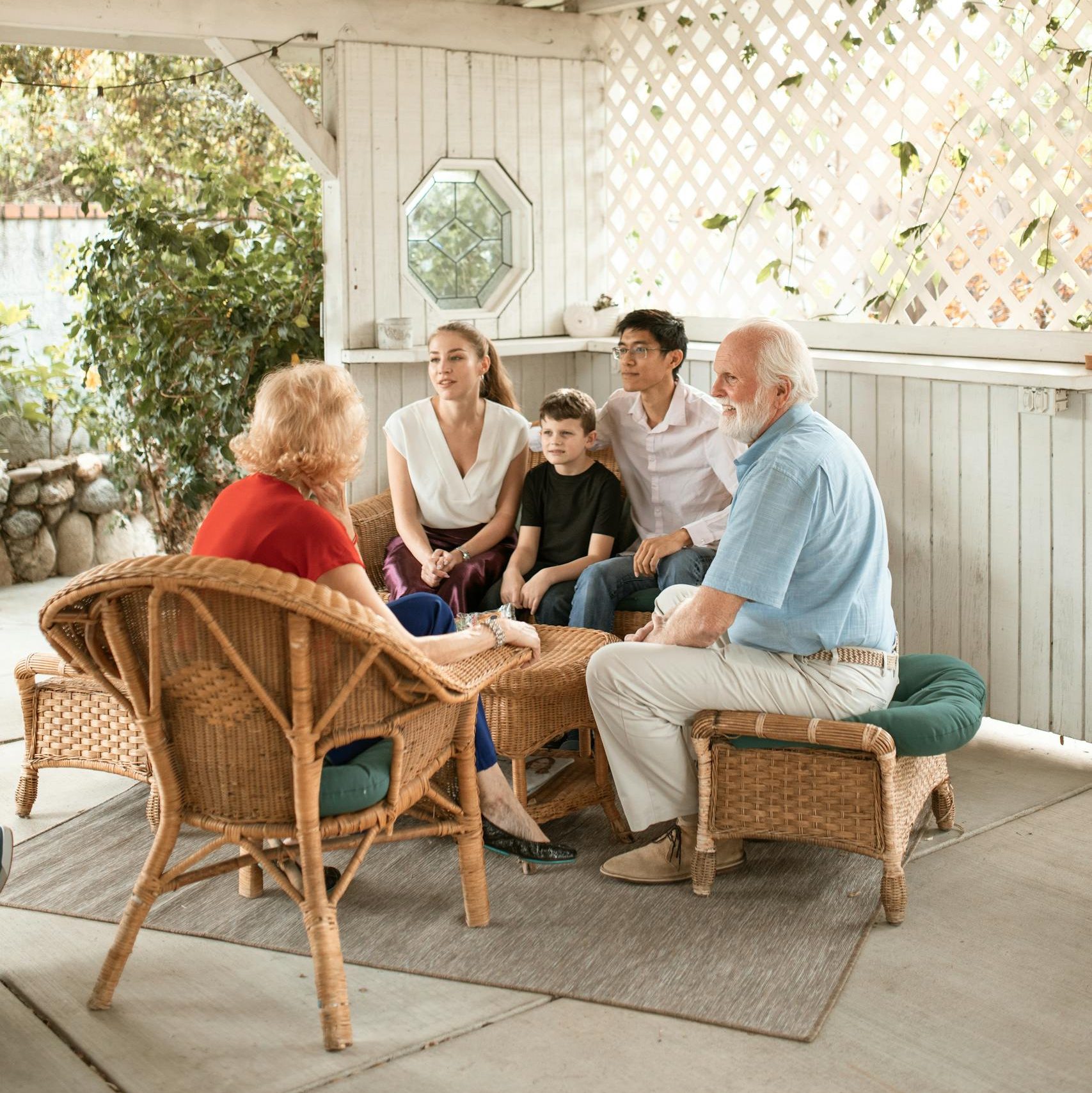 Family enjoys quality time together on cozy outdoor porch with wicker chairs.