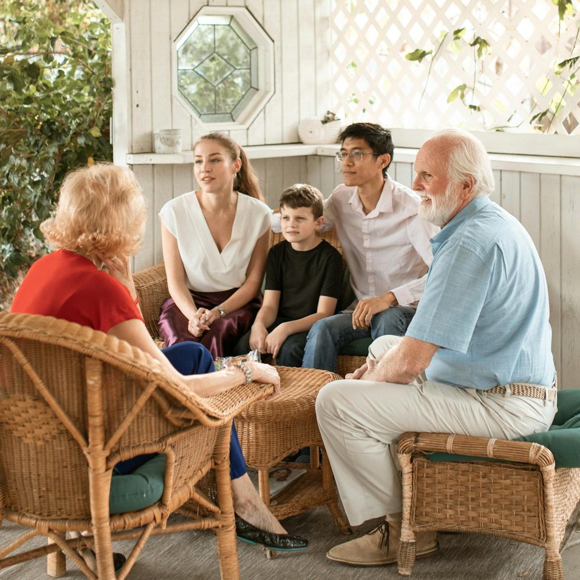 Family enjoys quality time together on cozy outdoor porch with wicker chairs.