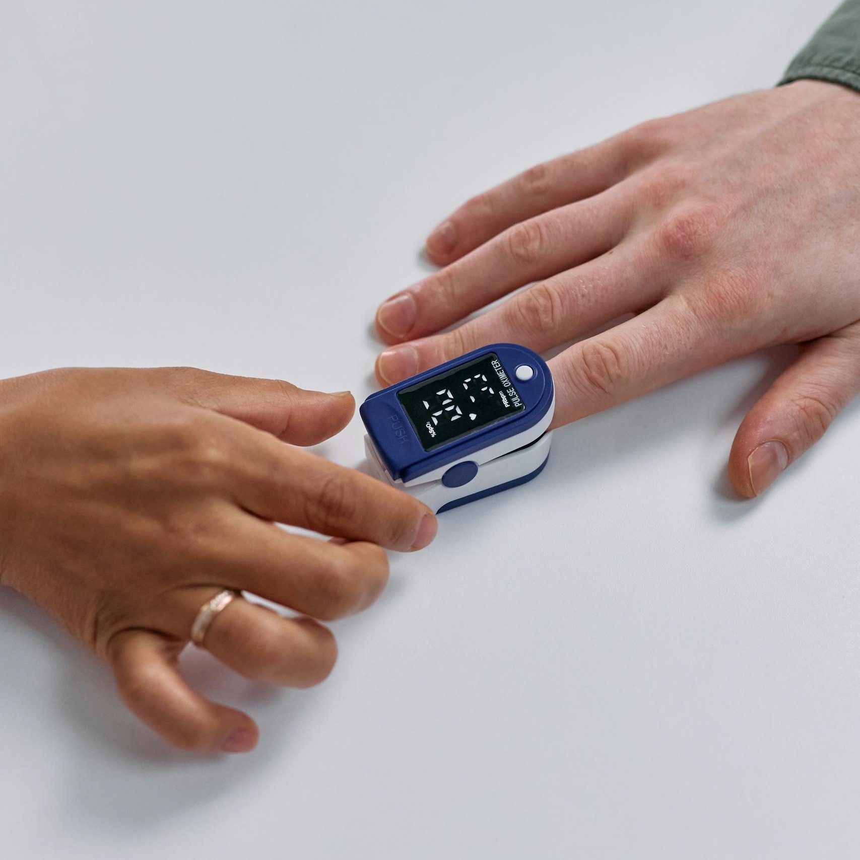 Close-up of a pulse oximeter on a person's finger, monitoring heart rate and oxygen levels.
