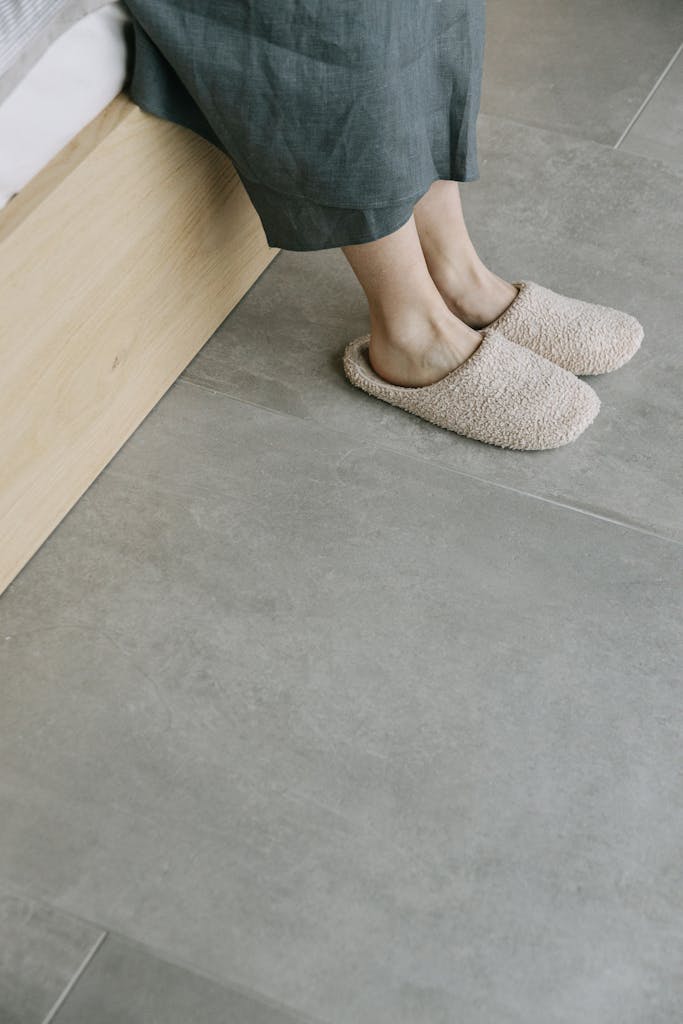 Close-up of a woman's feet in comfortable slippers sitting on a bed indoors.